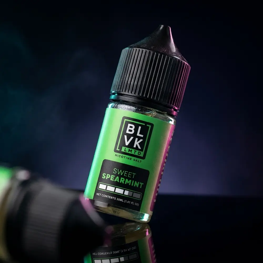 Frasco Líquido BLVK LMTD Sweet Spearmint sobre acrílico preto com iluminação cênica e reflexos - Vapor Gringo