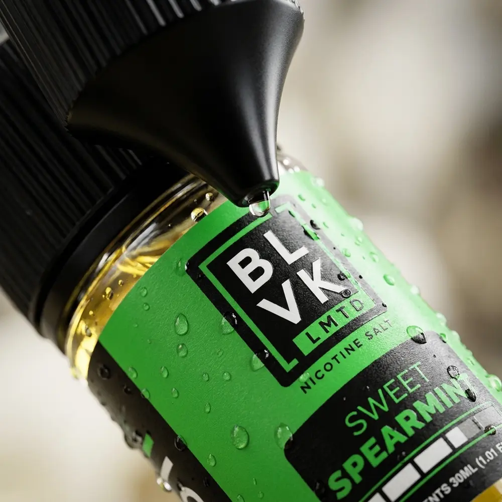 Detalhe macro do rótulo e bico do líquido BLVK LMTD Sweet Spearmint com gotículas e reflexos - Vapor Gringo
